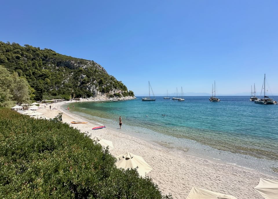 View from above of a white pebble beach with emerald water and a sailboat moored away from shore