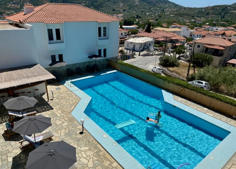 View overlooking a stone pool terrace and the red roofs of a Greek village