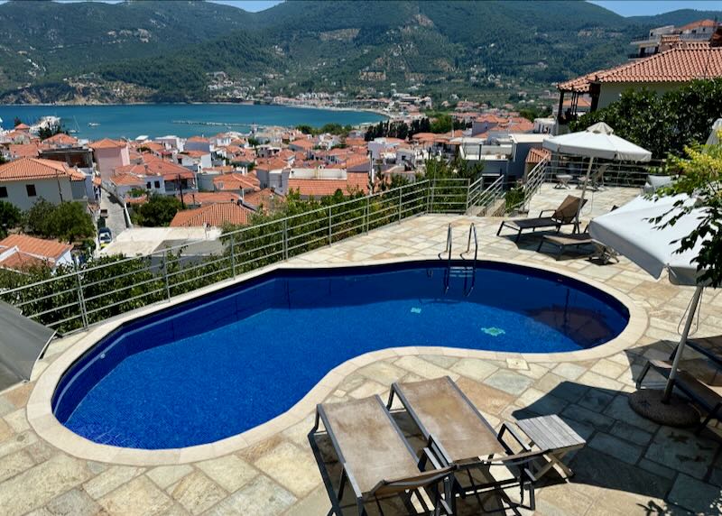 kidney-shaped swimming pool overlooking the red rooftops and olive groves of a Greek hillside village