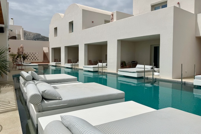 A long, shared pool lined wit double-sized sunbeds, all partially suspended over the water at Viva Nove hotel in Santorini.