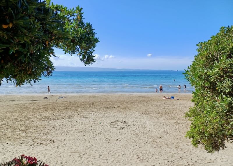 A few people lay in the sun on the sand at a beach.