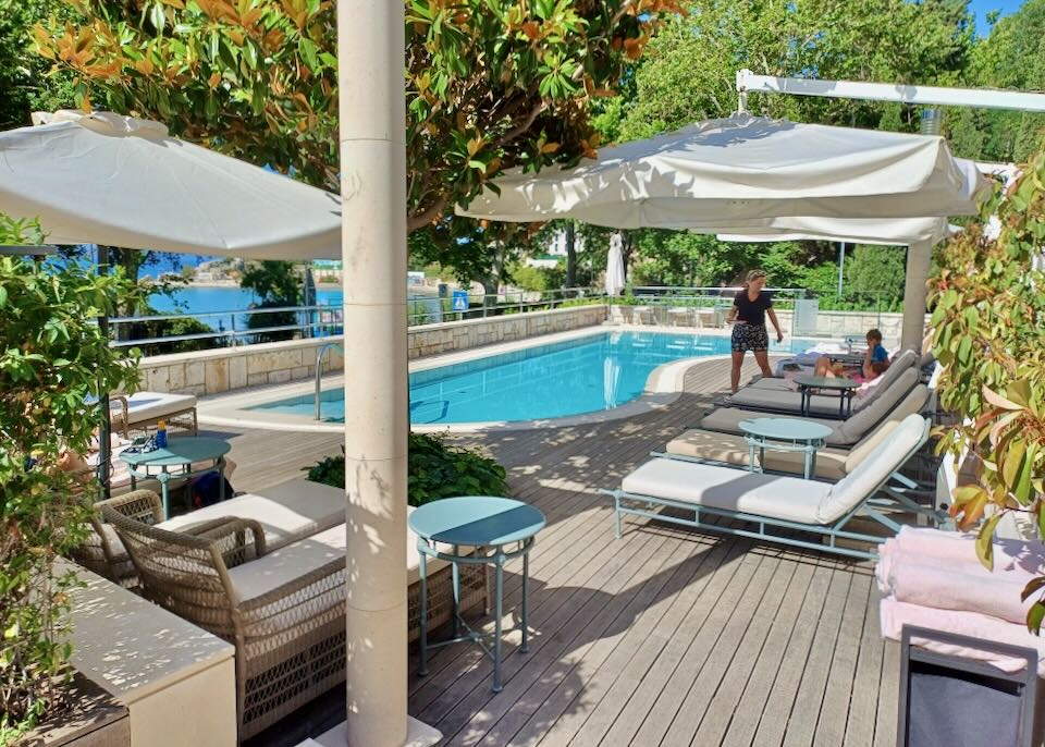 A woman walks by by a pool and her children sitting on lounge chairs.