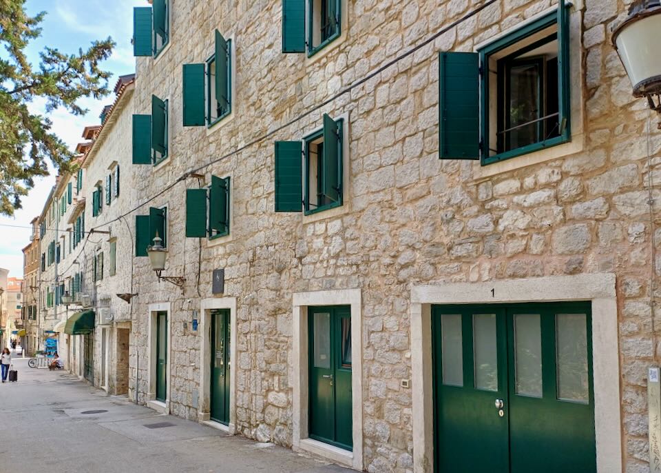 A cream-colored stone brick wall with green doors and shutters.