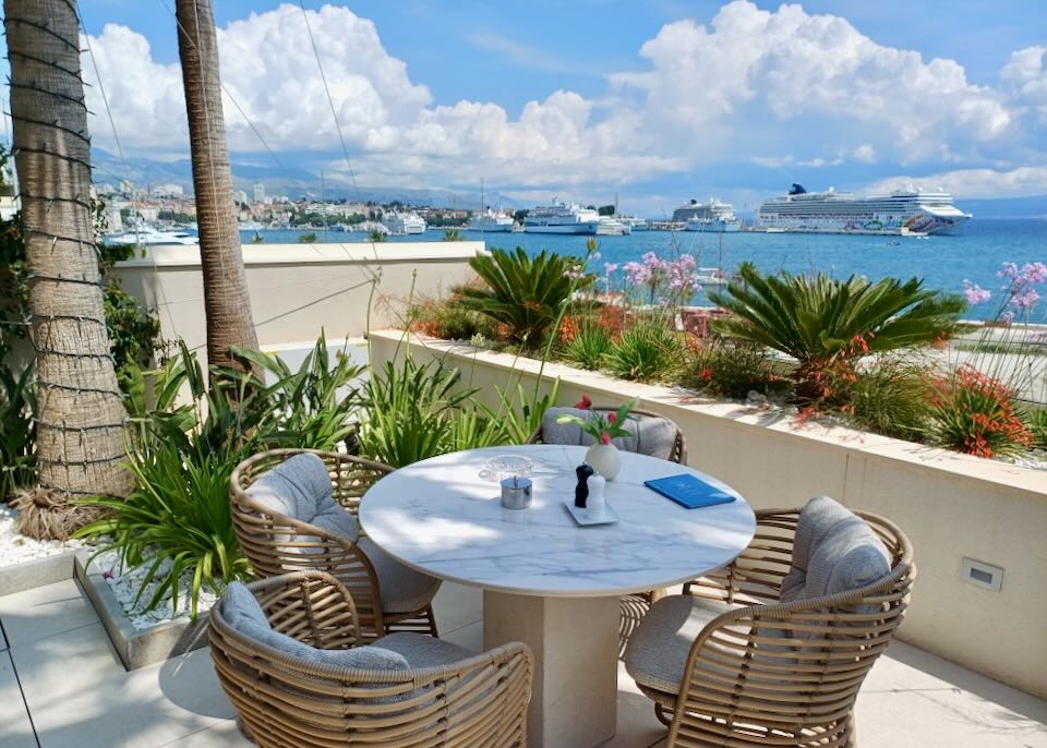 A table and chairs sits in the shade next to the sea.