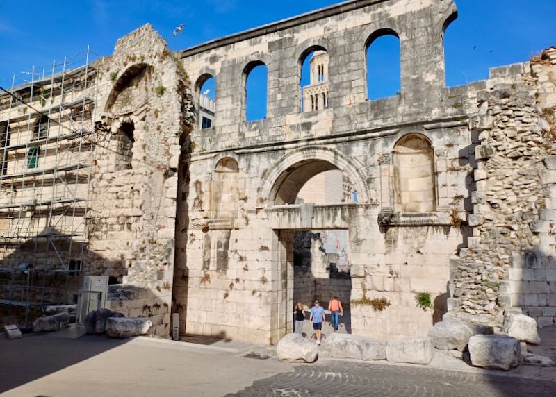 A couple walks through the ruins of tall old walls.