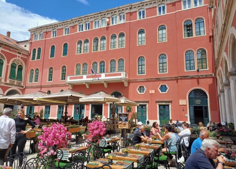 A red-painted building sits in the sun next to an outdoor dining area.