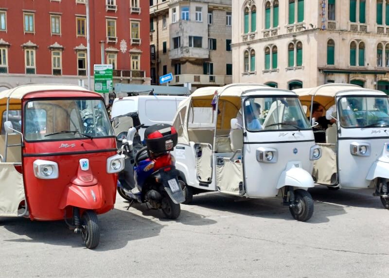 Three wheeled covered tuk tuks sit in a row.