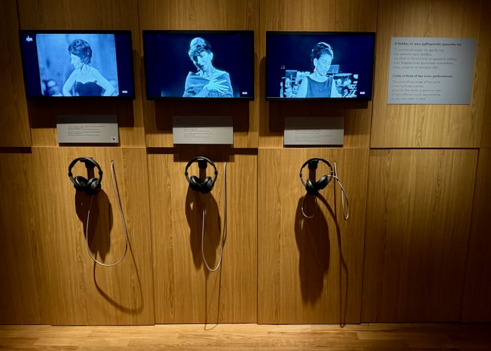 Listening stations mounted on a wall, with headphones and screens to watch an opera performance.