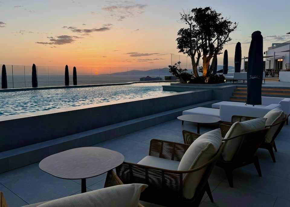 An infinity pool with a view of the sun setting into the sea at Deos in Mykonos Town.
