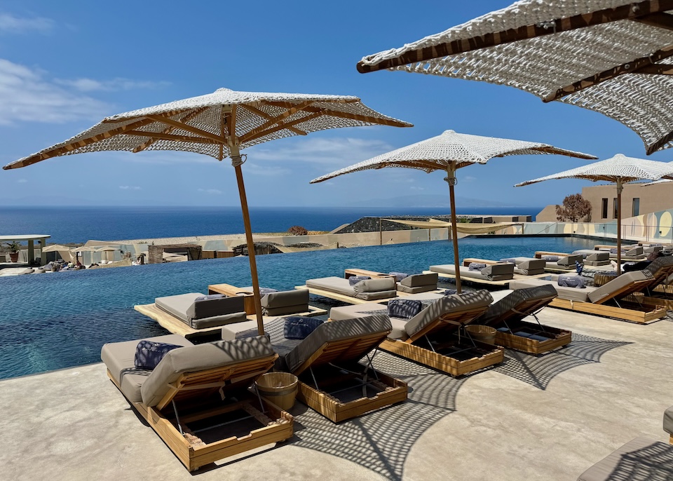 An infinity pool and two rows of sunbeds with macrame umbrellas face the Aegean Sea at Andronis Arcadia in Oia, Santorini.