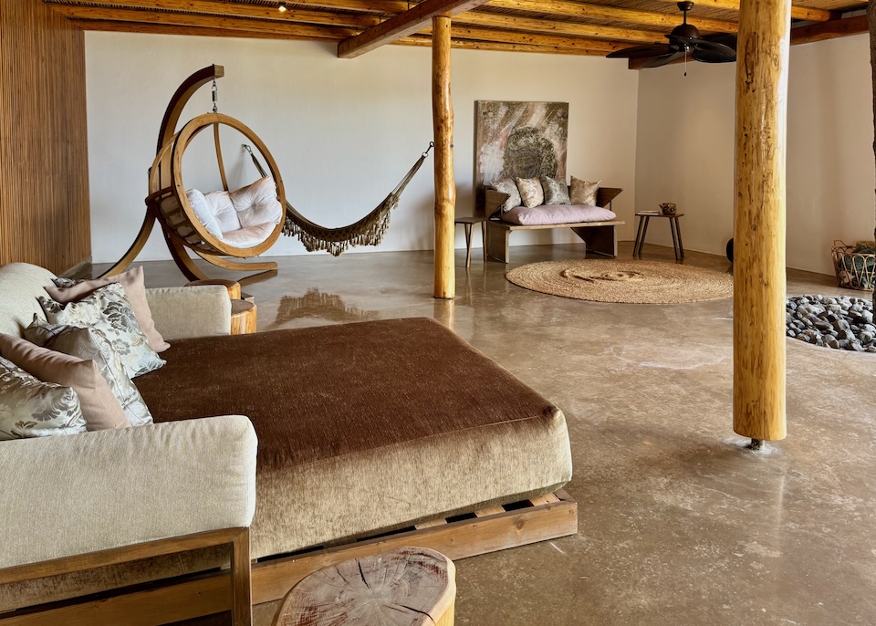 A plush, double-sized, chaise lounge, a hanging egg chair, and a hammock in the wood-ceilinged, stone-floor spa of Andronis Arcadia in Oia.