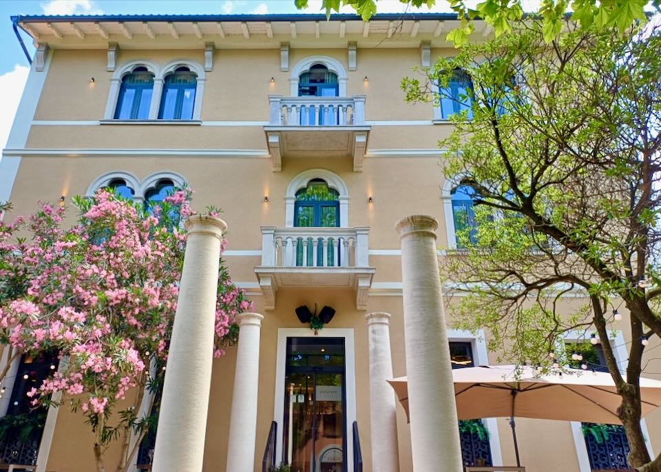 A three-story building with pillars sits in a garden.