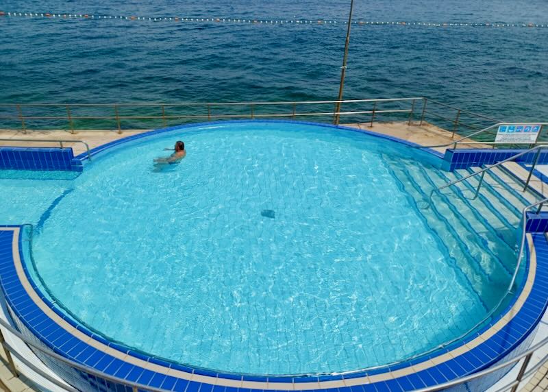 A man floats in a swimming pool by the sea.