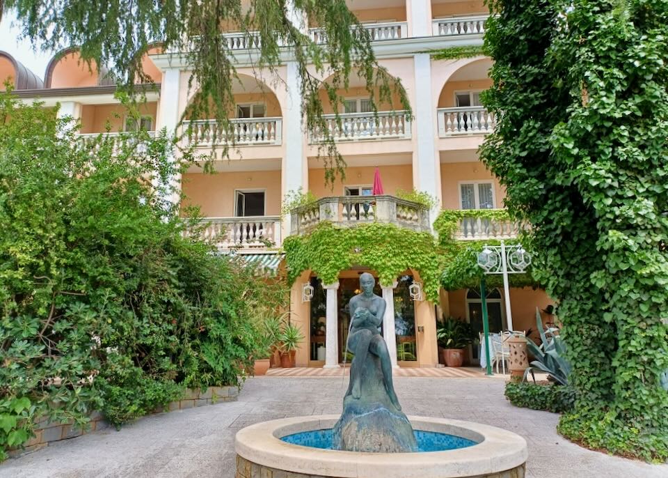 A fountain of a woman sits in front of a peach-colored hotel.