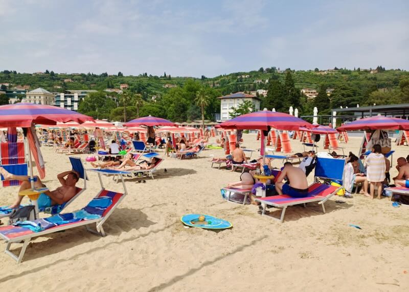 At a beach people sit on rented chairs under umbrellas.