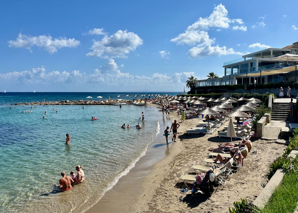 Rows of sun beds on a sandy beach in front of a tiered hotel dining terrace