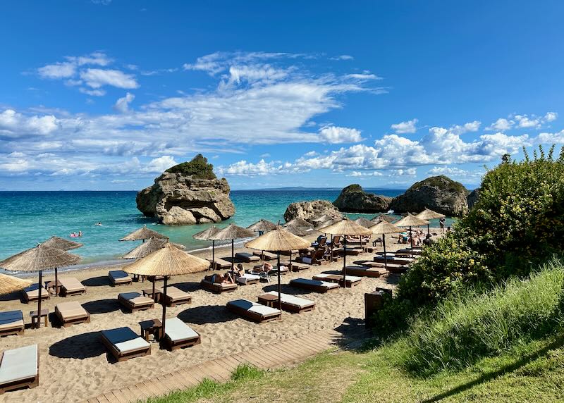 View of a golden beach with thatched sun umbrellas and craggy rock formations