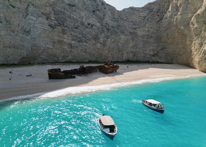 Photo of a decaying shipwreck sunk into golden sand in an Ionian Sea cove