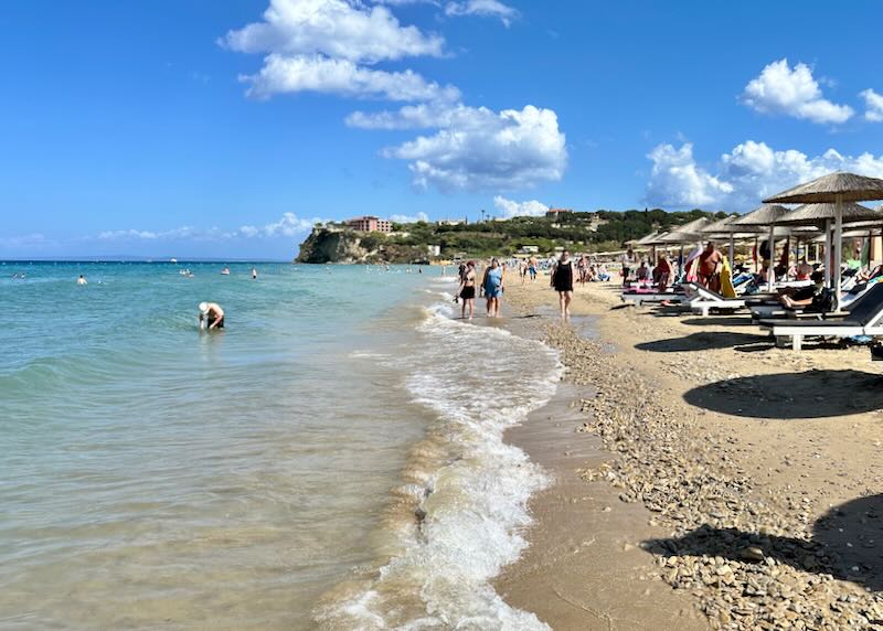 A man crouches in the surf at a golden sand beach on a sunny day.