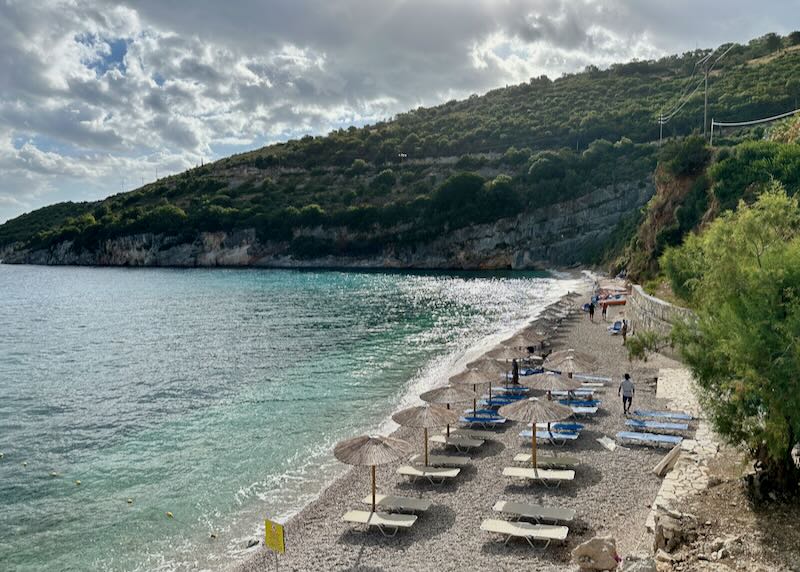 Overhead view of a pebble beach with sun loungers and a verdant cliff rising behind.