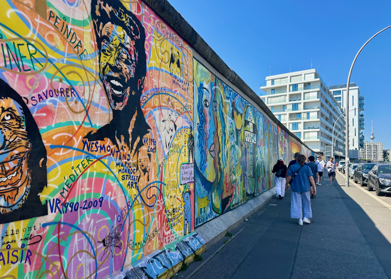 People walk along a large section of mural-covered wall in Berlin