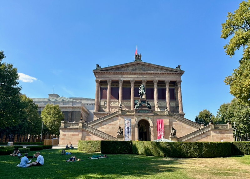 Pink Neoclassical building, with people lounging on the grass in front