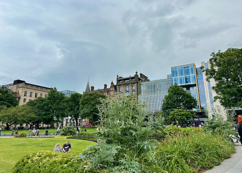 Green parkspace backed by a mixture of gothic and modern buildings 