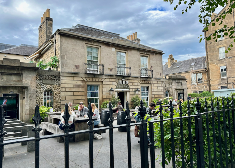 People eating at tables in a garden courtyard of an old stone building