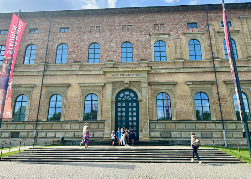 Exterior of a brick museum building, with people posing for a photo on the front steps