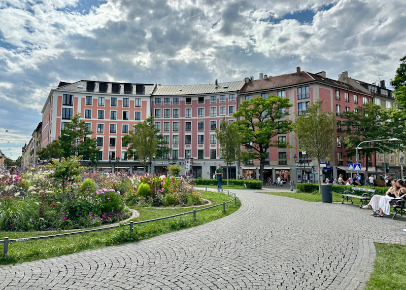 Curved gravel path leading past manicured gardens in a public park liked with colorful bavarian buildings