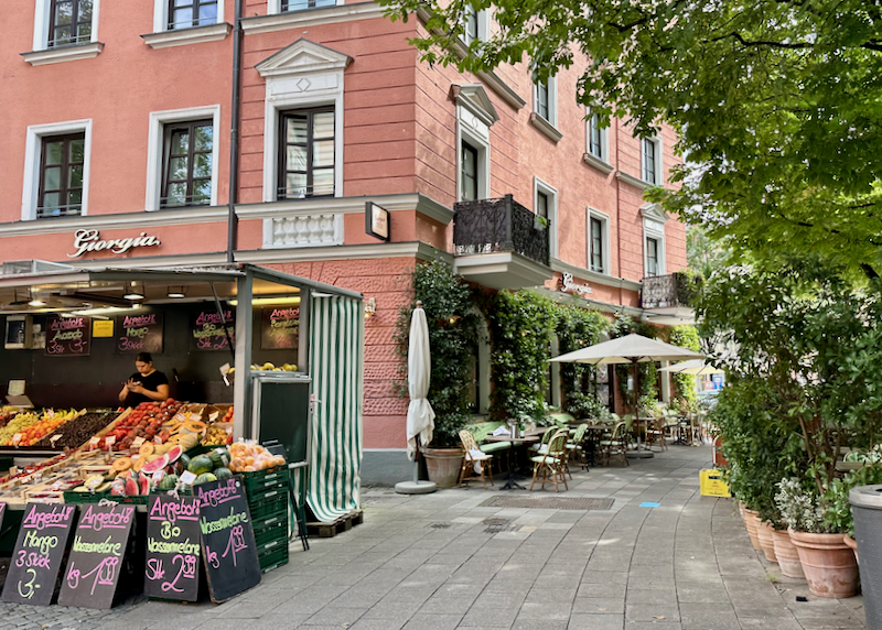 Picturesque corner in the Au-Haidhausen district of Munich, with a fruit stand and shaded cafe tables.