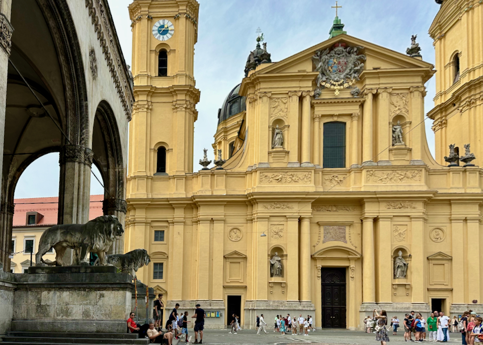 A grand saffron-colored building, looked over by a statue of 2 lions.