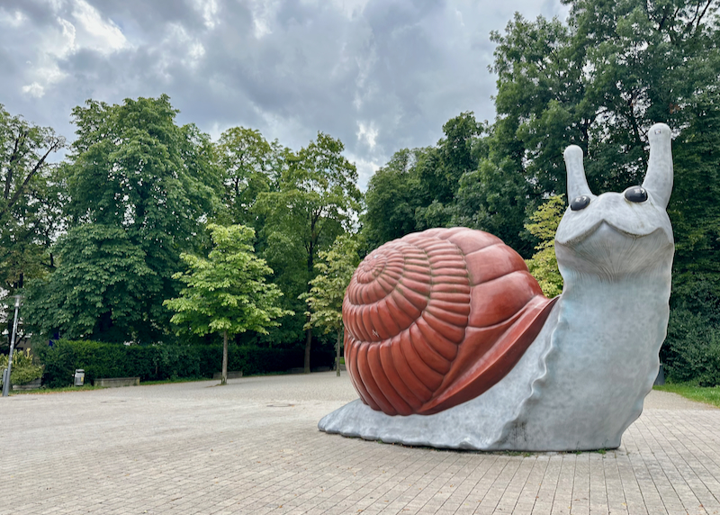 A large statue of a snail with red shell in a park setting.