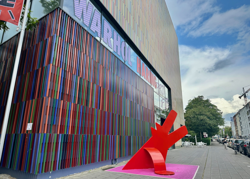 Exterior of a modern art museum, with a red Keith Haring sculpture in front
