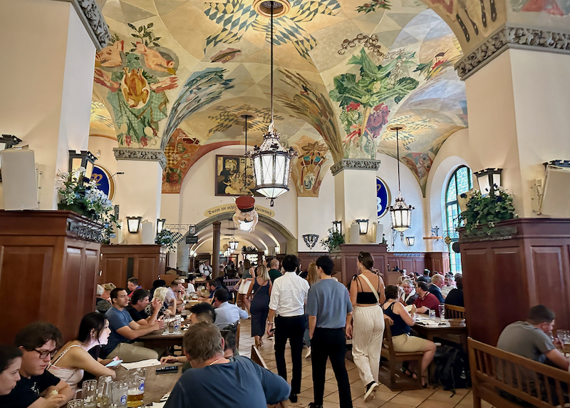Interior of a Bavarian restaurant with painted, coved ceilings and rustic tables.