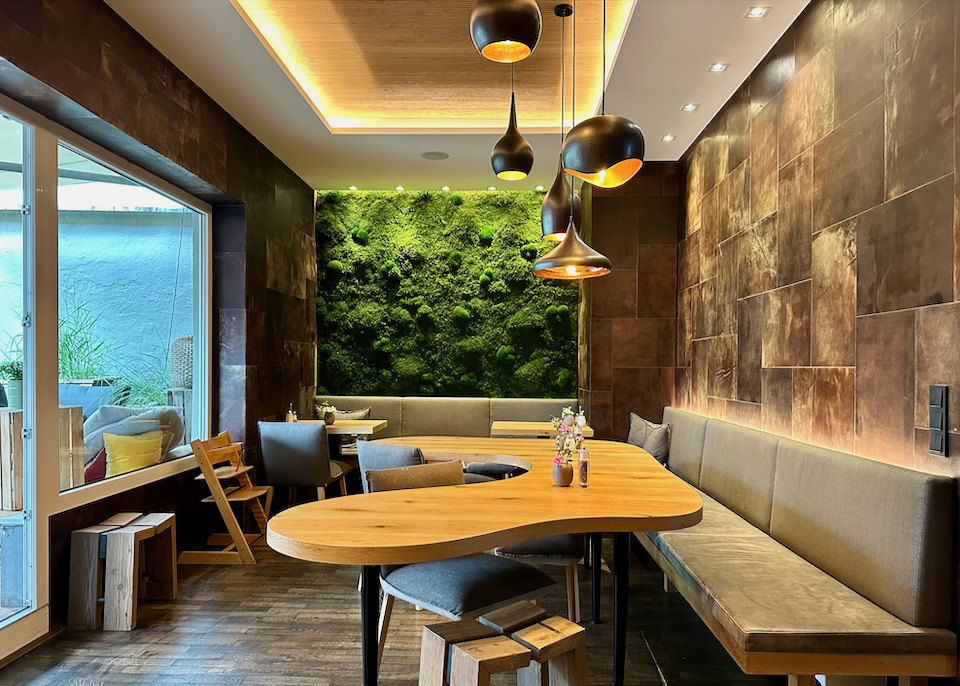 Hotel breakfast room with banquette seating, a freeform wood table, and a living wall covered in plants.