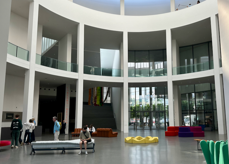 Modern, curved museum atrium, with people sitting on benches