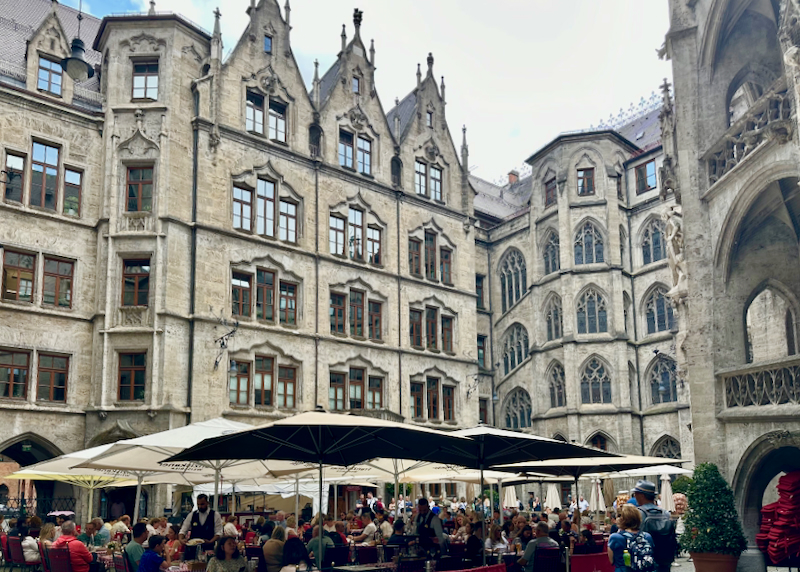 People dine at outdoor tables covered with umbrellas surrounded by gothic buildings