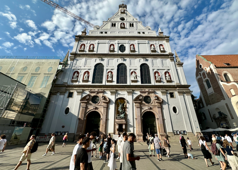 People walk in front of an ornate church in Munich.