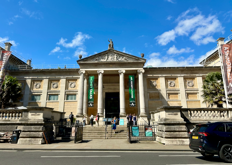 People sit on the front steps of the Ashmolean Museum in Oxford, England