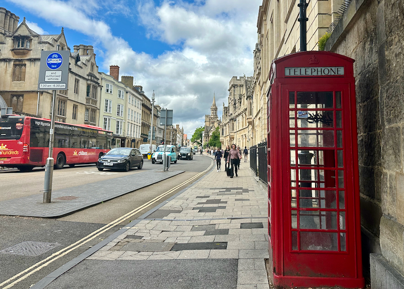 Pedestrians walk along a street in Oxford, England, with an old-fashioned red phone box in the foreground