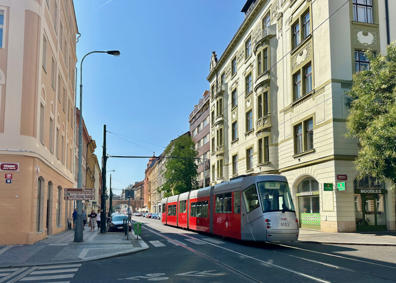 A red, modern streetcar passes through an intersection in Prague