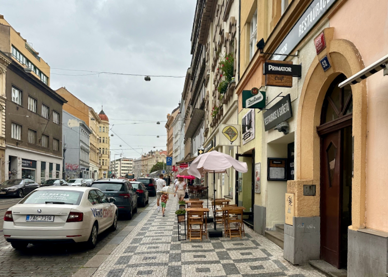 People with umbrellas walk down a mosaic-tiled sidewalk in Prague on a rainy day