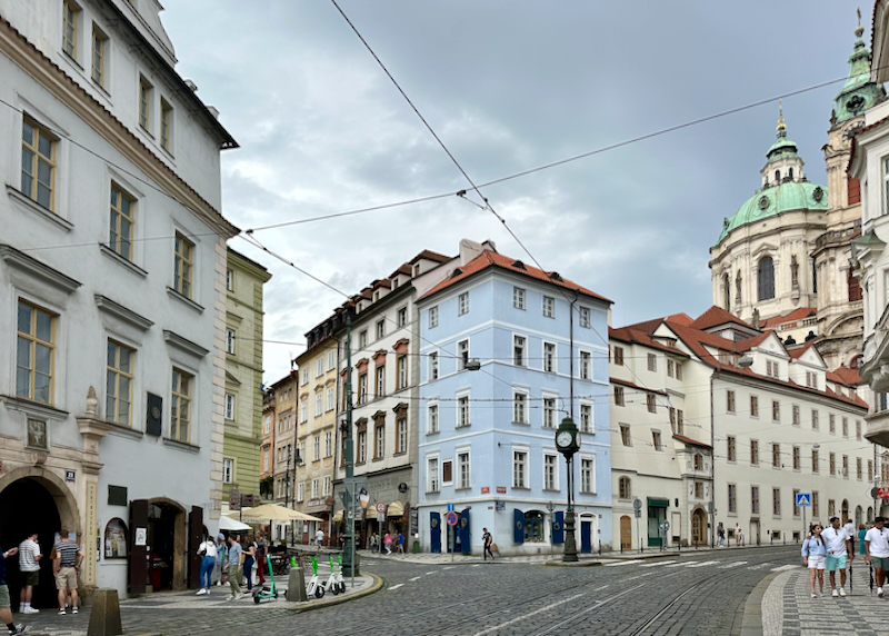 Colorful buildings on a Prague street corner, with a cathedral dome looming in the background 