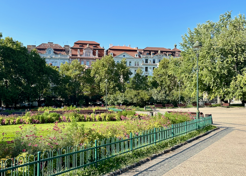 A well-manicured park in bloom, macked by stately Czech townhomes