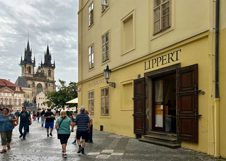 Exterior corner of Hotel Lippert in Prague, with pedestrians walking by and a castle in the distance 
