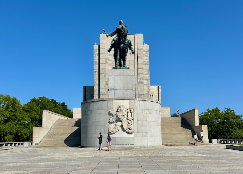 Tourists walk below a large bronze statue of a man on a horse