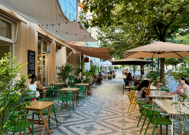 Umbrella-covered tables along a pattern-tiled sidewalk