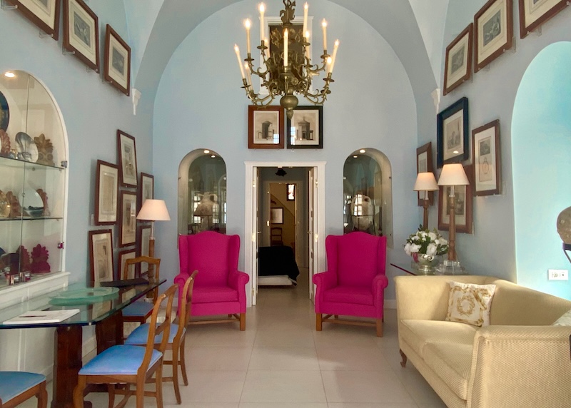 Refined furnishing and decor in a cave suite with sketches on the walls, a restored chandelier, and a case of antiques at The Tsitoras Collection hotel in Firostefani.