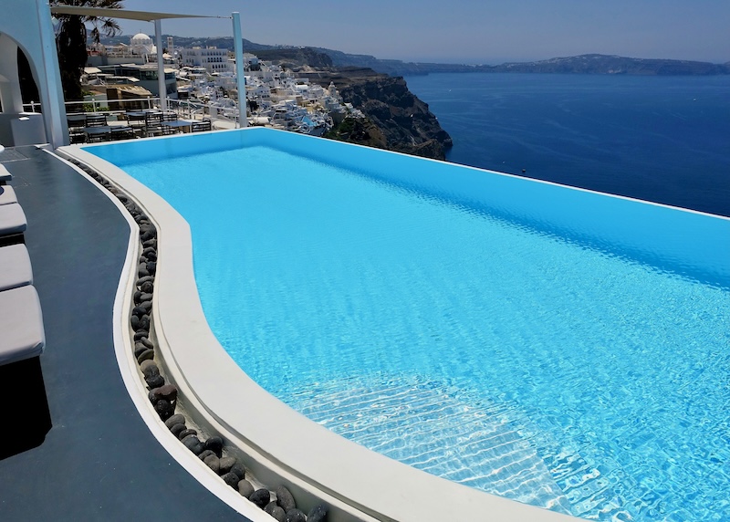 A freeform infinity pool with views over the caldera and toward Fira village at Cosmopolitan Hotel in Santorini.